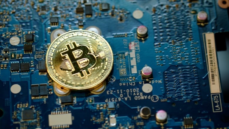 A gold Bitcoin coin sits on top of a computer chip. 
