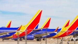 An image of two blue, yellow, and red Southwest planes with machines in the background and a barbed wire fence in front.